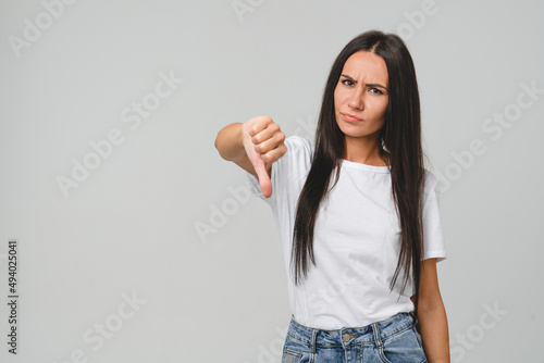 Negative opinion concept. Caucasian young woman in white T-shirt showing thumb down for unsatisfactory , bad quality concept isolated in grey background.