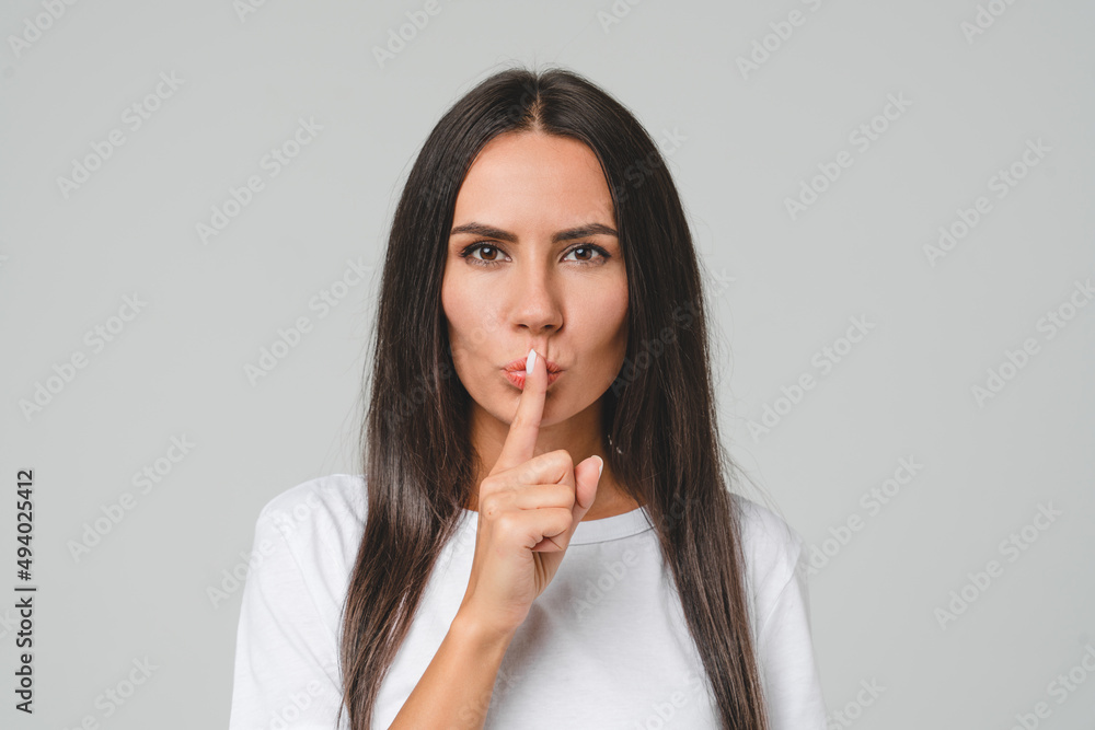 Top secret. Anonymous information. Caucasian young serious woman showing silent gesture, finger on lips, making hush isolated in grey background Top secret. Anonymous information. Caucasian young serious woman showing silent gesture, finger on lips, making hush isolated in grey background