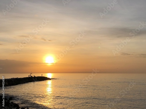 Orange sun over blue sea with fish men on the dark rocks © ruben