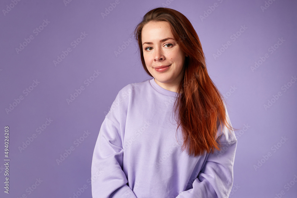 Caucasian woman in violet sweatshirt. Natural look. Smiling. long red hair. Violet background Caucasian woman in violet sweatshirt. Natural look. Smiling. long red hair. Violet background