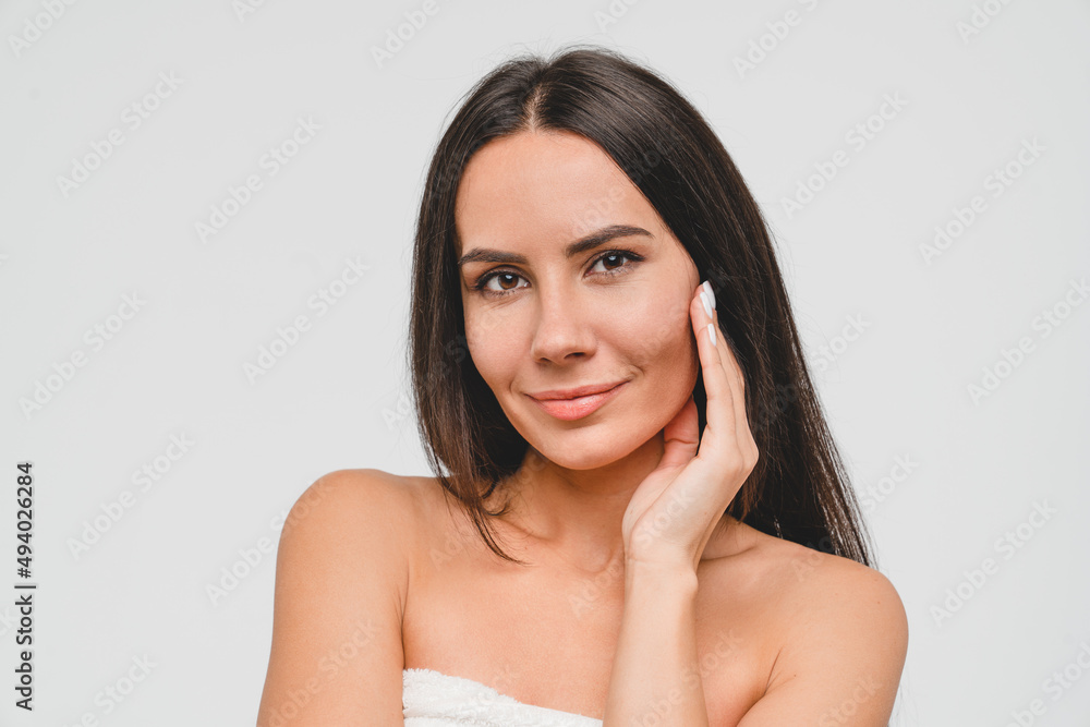 Good-looking young caucasian woman in bath spa towel with clear skin and healthy hair taking care of her beauty touching face isolated in grey background. Pampering and salon treatment Good-looking young caucasian woman in bath spa towel with clear skin and healthy hair taking care of her beauty touching face isolated in grey background. Pampering and salon treatment