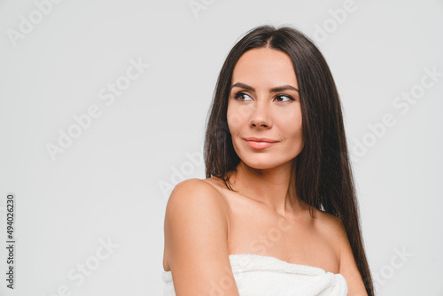 Pretty young caucasian woman in bath spa towel with clear skin and healthy hair taking care of her beauty isolated in grey background. Pampering and salon treatment