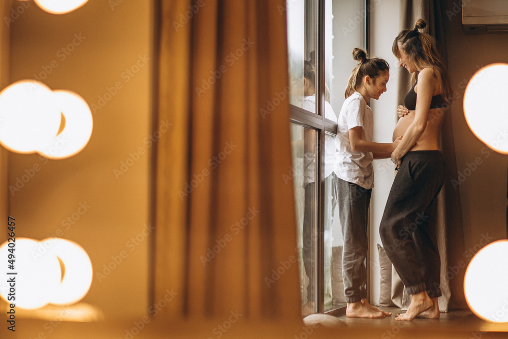 Pregnant woman standing with daughter by the window Pregnant woman standing with daughter by the window
