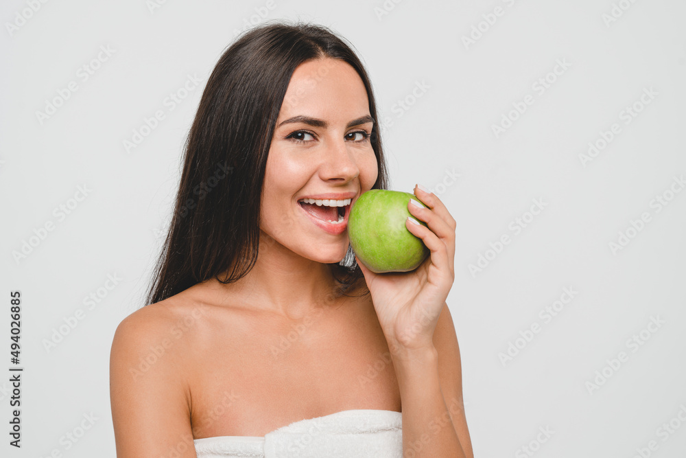 Caucasian young pretty woman girl female in bath spa towel eating green apple isolated in white background. Toothy smile, stomatology concept. Dermatology, clean skin care. Healthy eating dieting Caucasian young pretty woman girl female in bath spa towel eating green apple isolated in white background. Toothy smile, stomatology concept. Dermatology, clean skin care. Healthy eating dieting