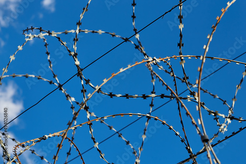 Circular barbed wire against blue sky, prison fence close up