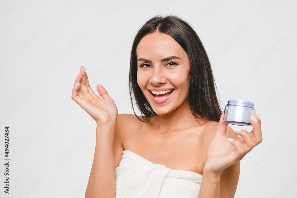 Pretty young woman apply facial cream looking at camera, beautiful healthy girl in spa bath towel put moisturizing lifting nourishing anti-age day creme on soft hydrated moisturized skin Pretty young woman apply facial cream looking at camera, beautiful healthy girl in spa bath towel put moisturizing lifting nourishing anti-age day creme on soft hydrated moisturized skin