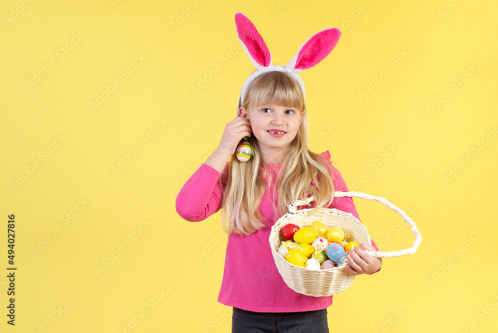 Cute little girl is holding a basket with Easter eggs. Yellow studio background Cute little girl is holding a basket with Easter eggs. Yellow studio background