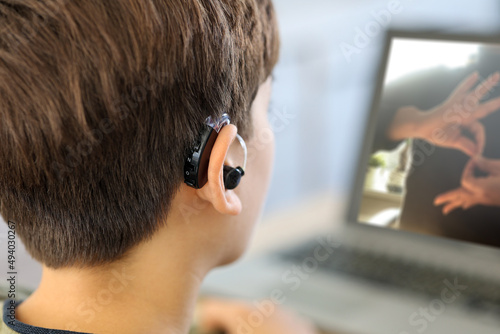 Deaf teenager boy Wearing Hearing Aid using Laptop. Disable student with disabilities deafness distancing learning online from home making communication hands language with teacher via VDO call.