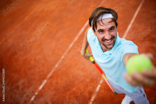 Young handsome tennis player with racket and ball prepares to serve at beginning of game or match. © NDABCREATIVITY