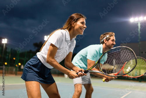 Beautiful young people are playing tennis as a team on tennis court outdoors. People sport concept © NDABCREATIVITY