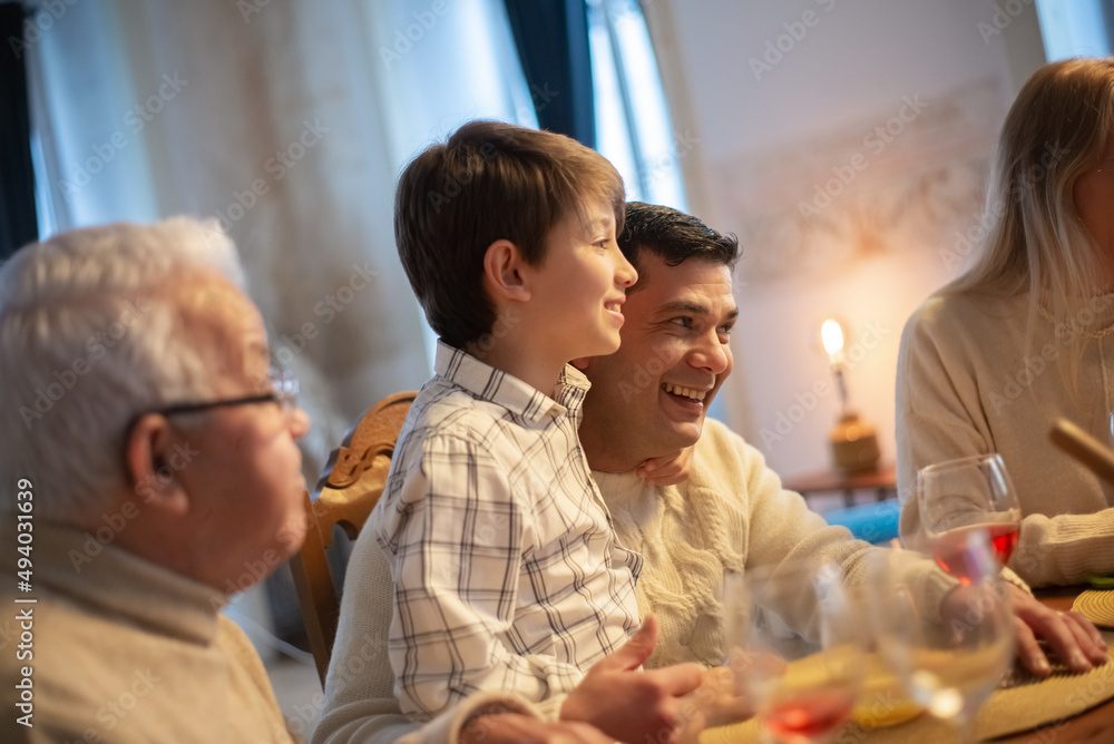 Happy father and his son laughing during family dinner. Multigenerational family sitting at table and having meal together. Family party concept