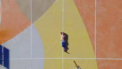 Young artist laying down outdoor with electric guitar on colorful playground field for football or basketball. music background, sport and music concept. Zoom out motion, zenit view, copy space.