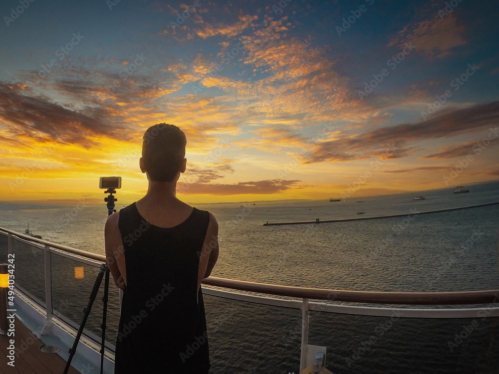Fototapeta premium Portrait of a young black male tourist on the deck of a cruise ship in front of a sunset sky. African tourist on the beach trip.