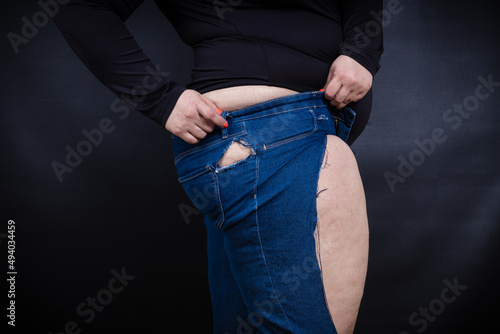 a fat woman puts on small jeans on herself on a black background photo