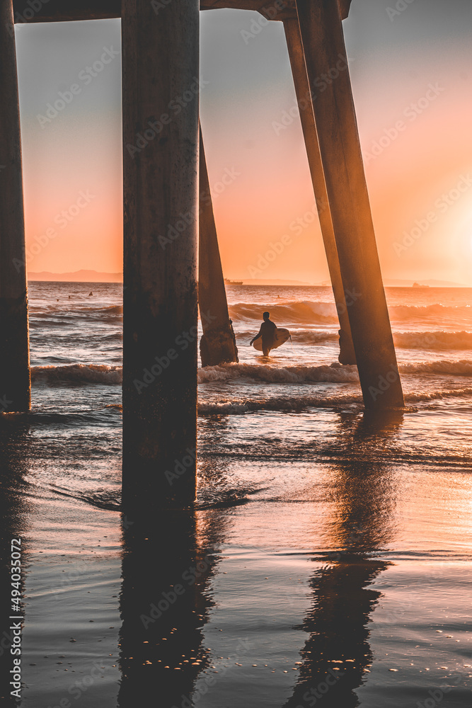 A surfer catching sunset waves under a Pier