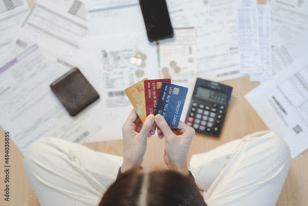 © Pormezz - Top view of stressed young asian woman trying to find money to pay credit card debt.