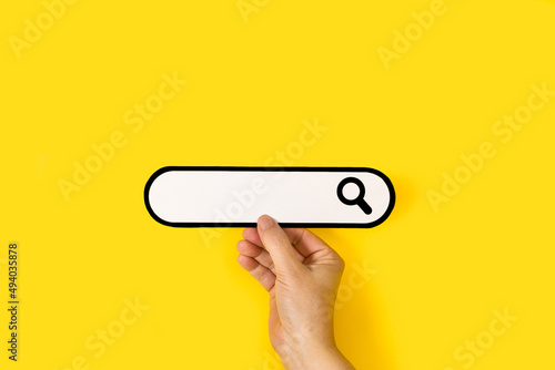 Mano de mujer sosteniendo un buscador de información sobre un fondo amarillo brillante liso y aislado. Vista de frente y de cerca. Copy space