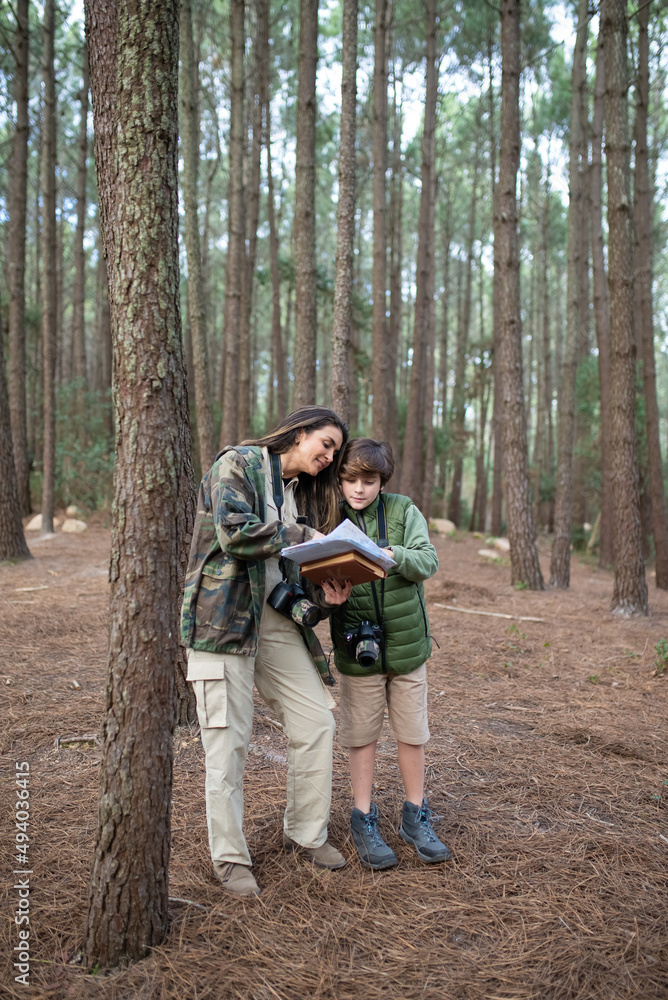 Happy family with cameras walking in forest. Dark-haired mother and son in coats getting ready to take pictures, discussing route. Parenting, family, leisure concept Happy family with cameras walking in forest. Dark-haired mother and son in coats getting ready to take pictures, discussing route. Parenting, family, leisure concept