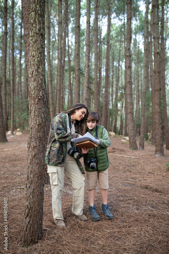 Happy family with cameras walking in forest. Dark-haired mother and son in coats getting ready to take pictures, discussing route. Parenting, family, leisure concept © KAMPUS