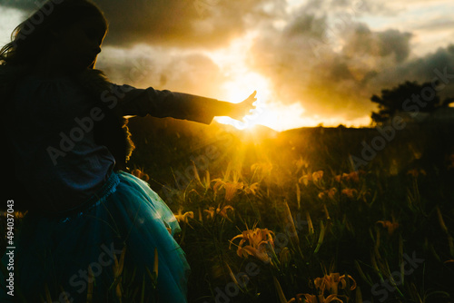 Girl reaches hand toward sunrays in flower field photo