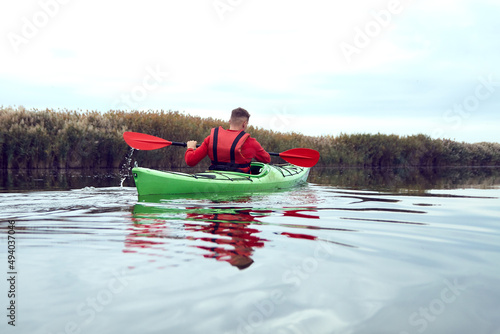 Rear view of man rowing in a green kayak in the river near bulrush at calm autumn day