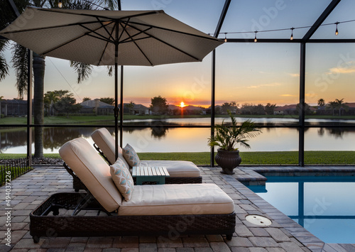 Florida screened swimming pool with lounge chairs overlooking lake at sunset