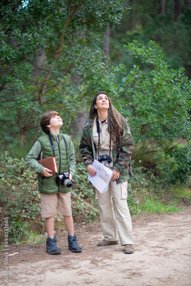 Happy boy and wo with cameras walking in forest. Dark-haired mother and son in coats getting ready to take pictures, looking up. Parenting, family, leisure concept Happy boy and wo with cameras walking in forest. Dark-haired mother and son in coats getting ready to take pictures, looking up. Parenting, family, leisure concept