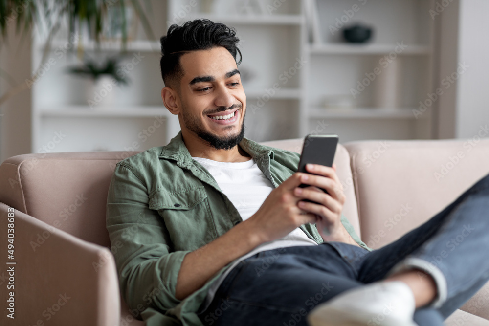 Portrait Of Handsome Young Arab Guy Relaxing With Smartphone At Home,
