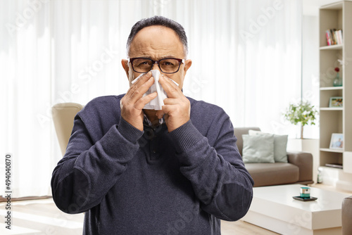 Mature man blowing nose with a paper tissue at home