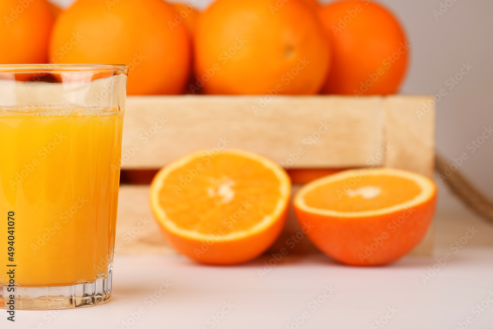 A glass of fresh orange juice, wooden box with rope handles full of fresh oranges, sliced orange on the side A glass of fresh orange juice, wooden box with rope handles full of fresh oranges, sliced orange on the side