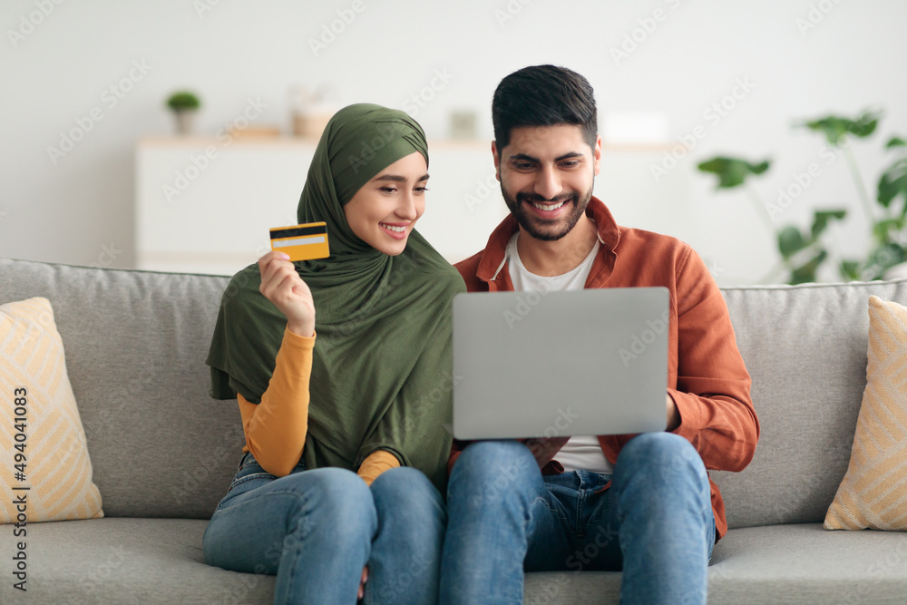 Muslim Couple Shopping Online Via Laptop And Credit Card Indoors Muslim Couple Shopping Online Via Laptop And Credit Card Indoors