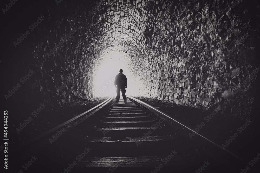 dark tunnel with a bright light at the end and the black silhouette of a man