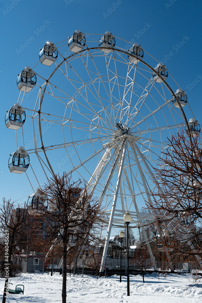 Ferris wheel with glass cabins, in the city park. Ferris wheel, photographed from below, on a wide-angle lens. Ferris wheel with glass cabins, in the city park. Ferris wheel, photographed from below, on a wide-angle lens.