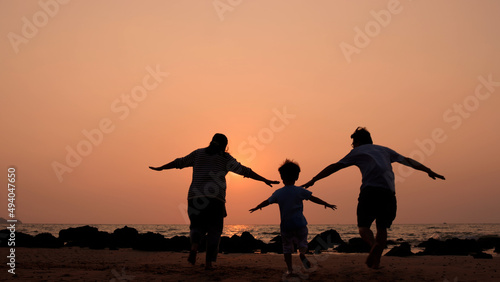Silhouette of happy Asian family having fun and running on the beach at sunset, Playing in summer and freedom travel concept
