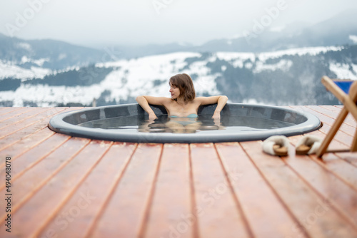 Billede på lærred Young woman bathing in hot tub at mountains during winter