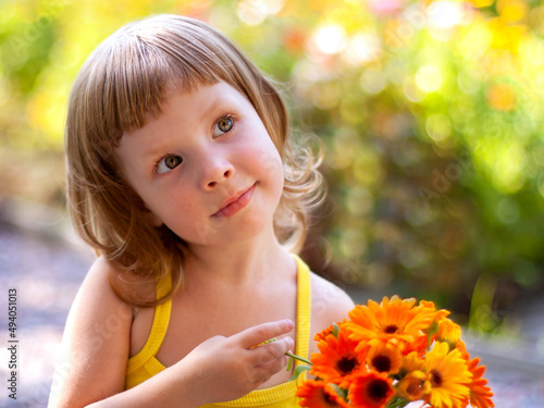 Cute little girl with a bouquet of flowers in the summer on the street carefully looks at someone