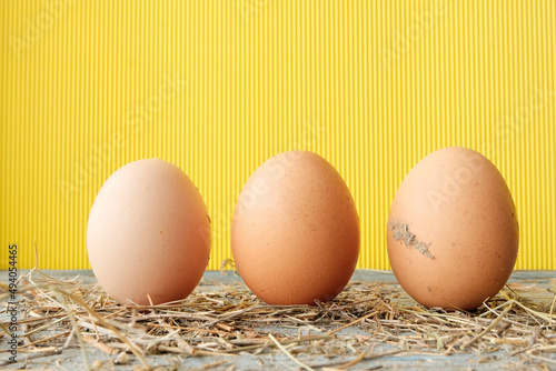 Large farm brown eggs on a wooden table, yellow background. Housekeeping concept, Easter holiday