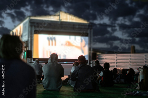 crowd of people watching a movie in the open air cinema at night