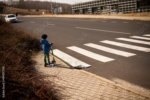 A five-year-old little Ukrainian boy stands in front of a pedestrian crossing with an electric scooter in Most city, Czech Republic.