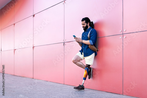 Man with artificial leg standing with smartphone in city