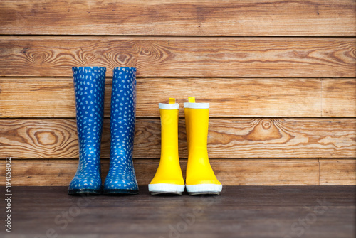 Blue and yellow rubber boots stand on the terrace. Adult and children's boots stand against the background of a wooden wall at home