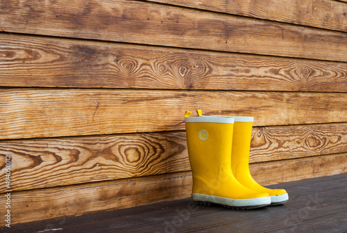 Children's yellow rubber boots stand on the terrace of a wooden house