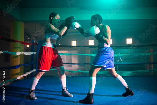 Side view of female boxers during boxing class. Two young girls training in gym with blue light, preparing for boxing match and practicing punches to win in bouts. Active sport, womens boxing concept