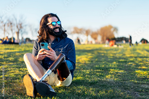 Cheerful man with bionic leg using smartphone on meadow