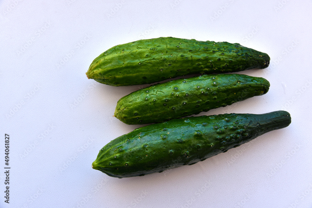 Three green fresh cucumbers on a white background