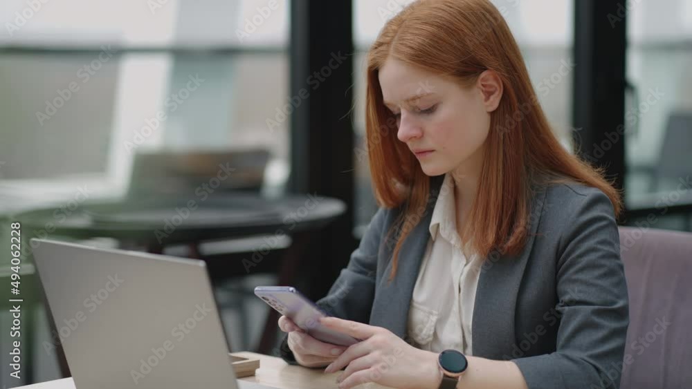 Young businesswoman use smart phone with laptop. Business woman in a modern office with a panoramic window, sunny day, laptop, tablet, use a mobile phone in a situation Young businesswoman use smart phone with laptop. Business woman in a modern office with a panoramic window, sunny day, laptop, tablet, use a mobile phone in a situation