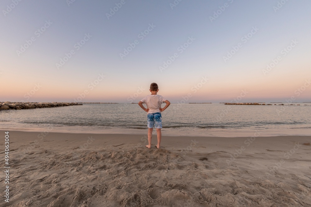 Child standing on the seashore at sunset looking at the horizon