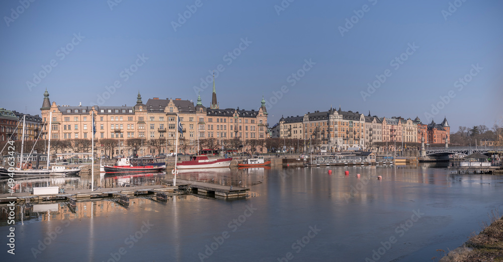 Panorama view over the pier at the district Östermalm, boats and jetties in the icy water of the canal Djurgårdskanalen in the bay Nybroviken a sunny spring day in Stockholm