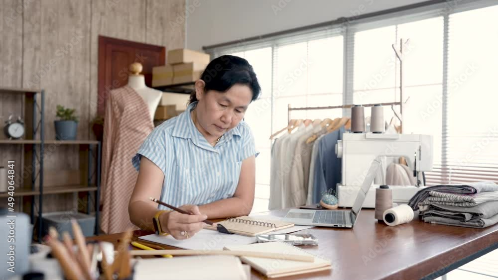 4K 50fps, Asian senior woman designing clothes to sell in her own shop in office, Professional small business owner in clothing design, Concept online store. 4K 50fps, Asian senior woman designing clothes to sell in her own shop in office, Professional small business owner in clothing design, Concept online store.