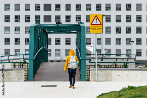 Woman with a yellow jacket walks towards a pedestrian walkway next to a yellow sign that says, do not cycle, danger of falling